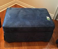 Front view of the dark blue wide ottoman on hardwood floor, showing the attached top cushion and skirted sides.