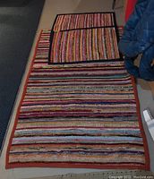 Three rag rugs stacked with stripes and colorful horizontal patterns. Two smaller rugs have labels showing silk and cotton composition.