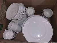 Box containing stacked white ribbed plates and cups