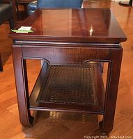 Photo showing front view of the wooden side table with figured grain top and woven rattan lower shelf, highlighting the East Asian style base design.