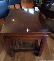 Front view of the wood side table showing the figured grain panel top and rattan shelf base with East Asian style legs.
