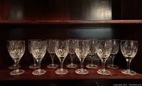 Front view of a row of twelve clear Stuart crystal cut wine glasses with detailed cuts and starburst bases.