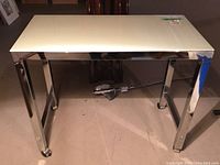Front view of chrome frame console table with white glass top on casters, showing reflective legs and glass surface.