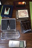 Photo of assorted travel accessories including metal cases, coasters with map designs, a digital travel clock, and metal flask with initials.