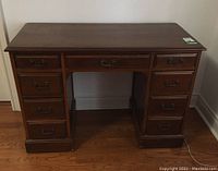 Front full view of the vintage solid wood desk showing seven drawers, dark stain, brass handles, and overall condition.