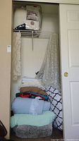 Closet with stacked folded comforters, blankets, lace table linens, and patterned bedding items.