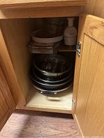 Inside cabinet showing stack of metal mixing bowls, glass measuring cups, ceramic baking pans, and a white manual food chopper.