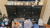 Front view of the black wooden cabinet showing two center drawers and decorative side doors. Surface has various items placed which are not included.