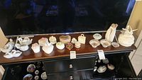 Overview photo showing all ceramic decorative items on top of a dark wooden cabinet, includes swan figurines, lidded boxes, small bowls, and a figurine of two figures embracing.