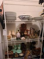 View of upper and middle shelves showing white china dinnerware, Limoges serving bowl, and various small decorative items including Avon pieces and anniversary clock.