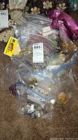 Several clear plastic bags filled with assorted costume jewelry including bracelets, rings, and necklaces in various styles and colors, placed on a carpeted floor.
