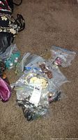Multiple plastic zip lock bags containing various pieces of costume jewelry spread on carpeted floor.