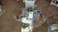 Overhead photo showing multiple plastic bags filled with assorted costume jewelry pieces including necklaces and bracelets on carpeted floor.