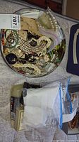 Photo of a round tin filled with various pieces of vintage costume jewelry including beaded necklaces and pearl strands