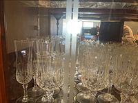 Front view of multiple crystal flutes and stemware glasses arranged inside a glass china hutch shelf, showing intricate cut glass patterns.