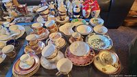 Overview of multiple assorted demitasse cups and saucers arranged on table showing variety and quantity.