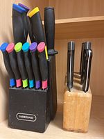 Black Farberware cutter block with seven knives visible, assorted color handles, plus one large black-handled knife, arranged in kitchen pantry shelf.