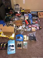 Photo showing a wide assortment of automotive-related parts and tools, including brake pads, Bosch plugs, and a grinder, laid out on the floor in a collection of boxes and plastic packaging.