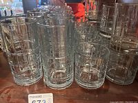 Multiple clear glasses of varying heights featuring a geometric grid pattern arranged on a wooden surface.
