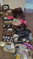 Image showing a group of over 20 assorted handbags and purses arranged on a carpeted floor, various styles, sizes and patterns visible