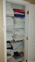 Closet shelf with folded towels, washcloths, and bedding stacked on five shelves.