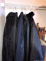 Five black outerwear coats hung on a white wire rack, showing different textures including faux fur and faux leather.
