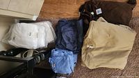 Multiple clothing items laid out, including beige and blue t-shirts, gray shorts, and white thermal tops in packaging.
