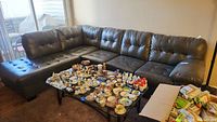 Front and side view of dark brown faux leather sectional sofa with multiple cushions, showing general condition and style, with many small dishware items on table in front for size context.