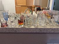 Front view showing multiple clear glass shot glasses including a Hard Rock Cafe shot glass, a glass with '43' logo, and others with various prints.