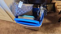 Large storage totes, beige and blue, stacked and filled with various items including baskets and grocery totes.