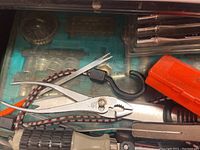 Top view of metal pliers, orange handled screwdriver, and hooks inside plastic tool organizer.