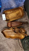 Three wooden serving trays on carpet: large rectangular tray, boat-shaped tray with compartments, uniquely shaped divided tray.