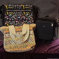 Overall view of three bags: Bongo double flap messenger bag with multicolor doodle print, floral lined canvas tote bag, and Ricardo black canvas travel bag