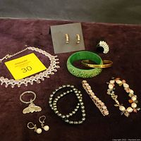 Costume jewelry lot showing pink crystal beaded choker, assorted bracelets, earrings, cocktail ring, and metal bee key ring on brown surface.