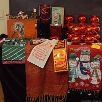 Collection of red mercury glass vases, bauble stands, vintage boxes, ornaments, cloth table runners and gift bags arranged on a black cloth surface.