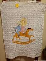 Full view of offwhite quilt with appliqué of two children on gold rocking horse