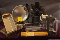 Photo showing arrangement of kitchen tools, cake pans, bread pans, glass container, French press, glass pitcher, and silicone baking mat.