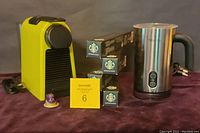 Photo showing bright green Nespresso Essenza Mini Espresso Machine, stainless steel Sboly milk frother, and four unopened boxes of Starbucks espresso pods.