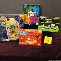 Four board and card games arranged together: Snake Oil, Dead Last, The Oregon Trail card game, and In a Pickle. Three are new and sealed, one is opened but unused.