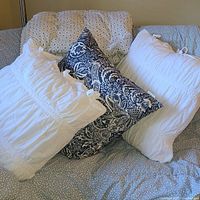 Three oversize decorative pillows arranged on a couch: two white shirred with ties and one blue and white patterned pillow, showing size and fabric texture.