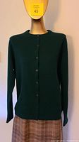 Front view of dark green cashmere cardigan buttoned up over light brown plaid skirt on mannequin