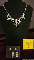 Vintage La-Rel 15-inch rhinestone necklace displayed on a black bust with two pairs of rhinestone earrings placed below it on a black stand. A MaxSold number card is nearby.