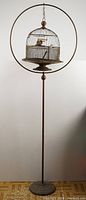 Full view of round domed bird cage hanging from circular hoop on metal stand