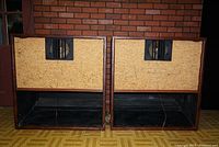 Rear view of two vintage Gabriel IV stereo speakers showing speaker drivers and vent ports with protective grills and light fabric panels with visible wear and splits.