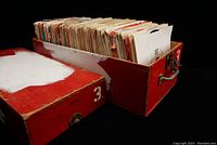 Open red and white wooden box filled with 45 RPM vinyl singles