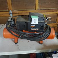 Side view of orange tank air compressor with black motor housing and black air hose coiled on top.