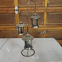 Three metal lantern tea light holders arranged on a white table with a wooden wall background, showing the overall design and condition.