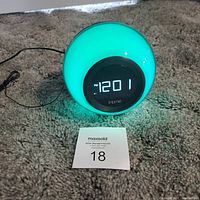 Photo of the front of the spherical iHome Bluetooth alarm clock showing digital time display and glowing teal color light.