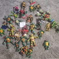 Photo of approximately 22 Teenage Mutant Ninja Turtles action figures arranged on carpet showing variety of characters and styles.