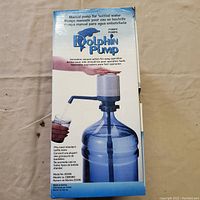 Box displaying Dolphin Pump brand manual pump for bottled water, showing usage on a large 3 to 5 gallon water bottle, multilingual text on packaging.